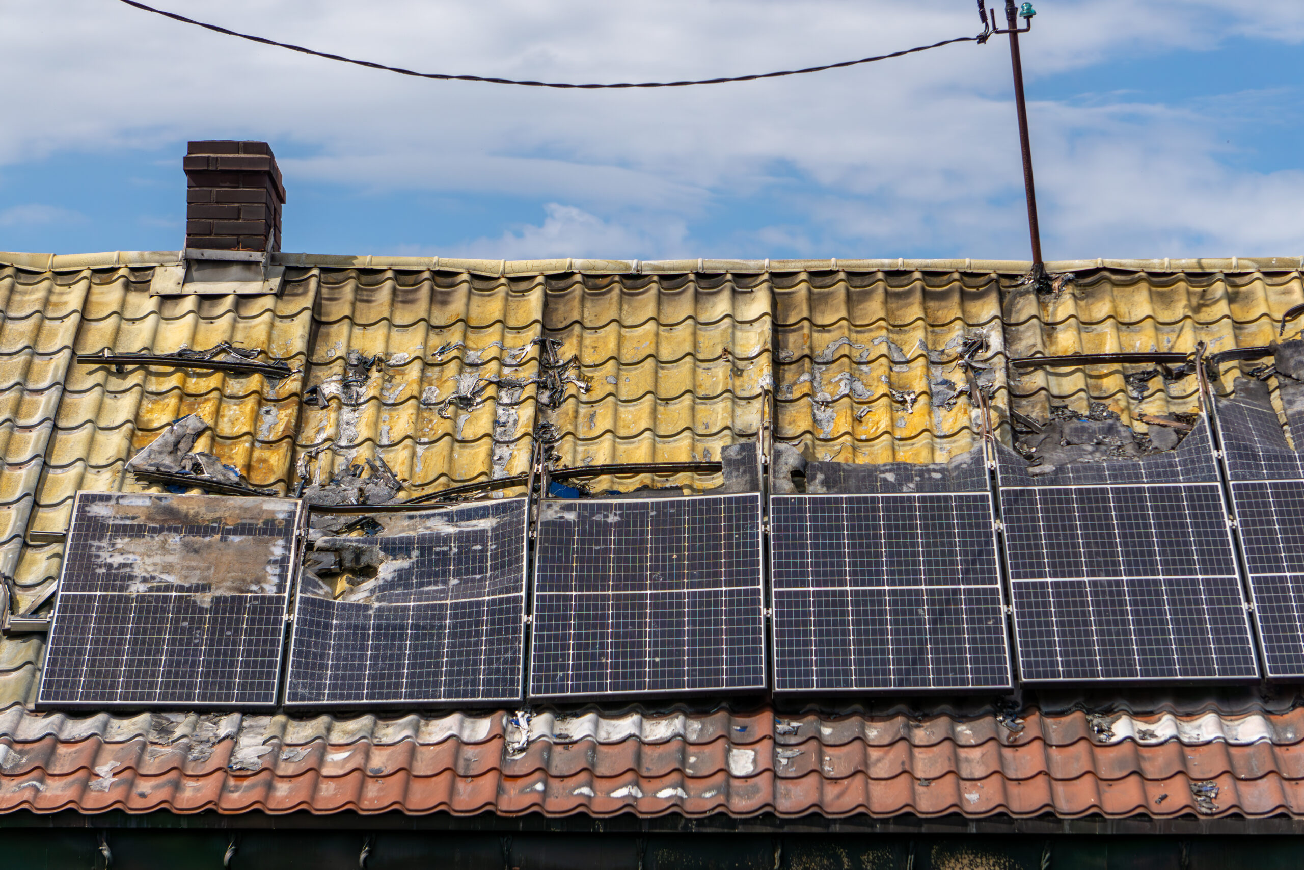 Burnt building roof after fire – damaged solar panels and scorched roof tiles with visible fire damage.