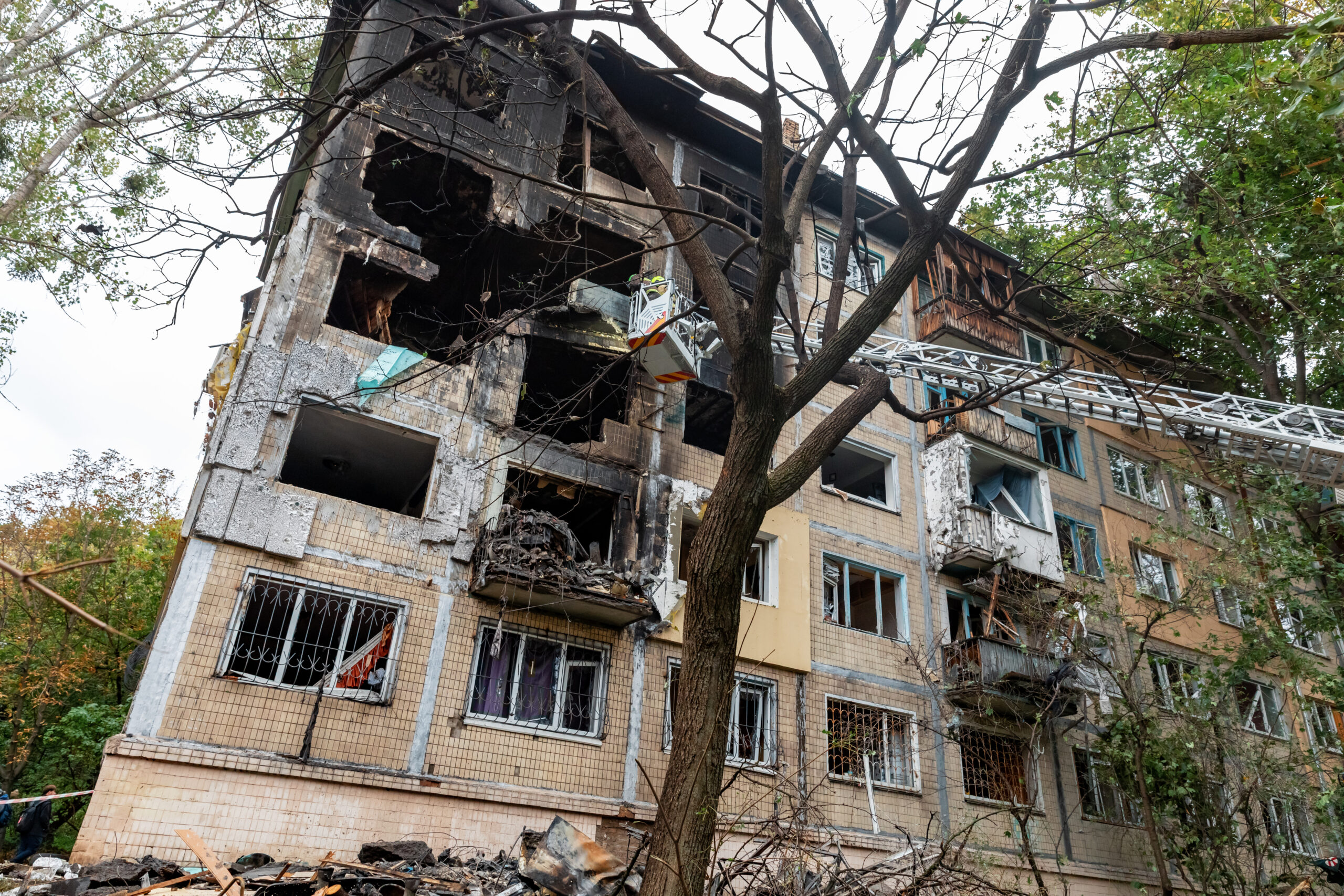 Extensive burn damage and structural destruction to the corner of a Kyiv residential building following a Russian air attack is seen, with a visible rescue ladder assisting cleanup.