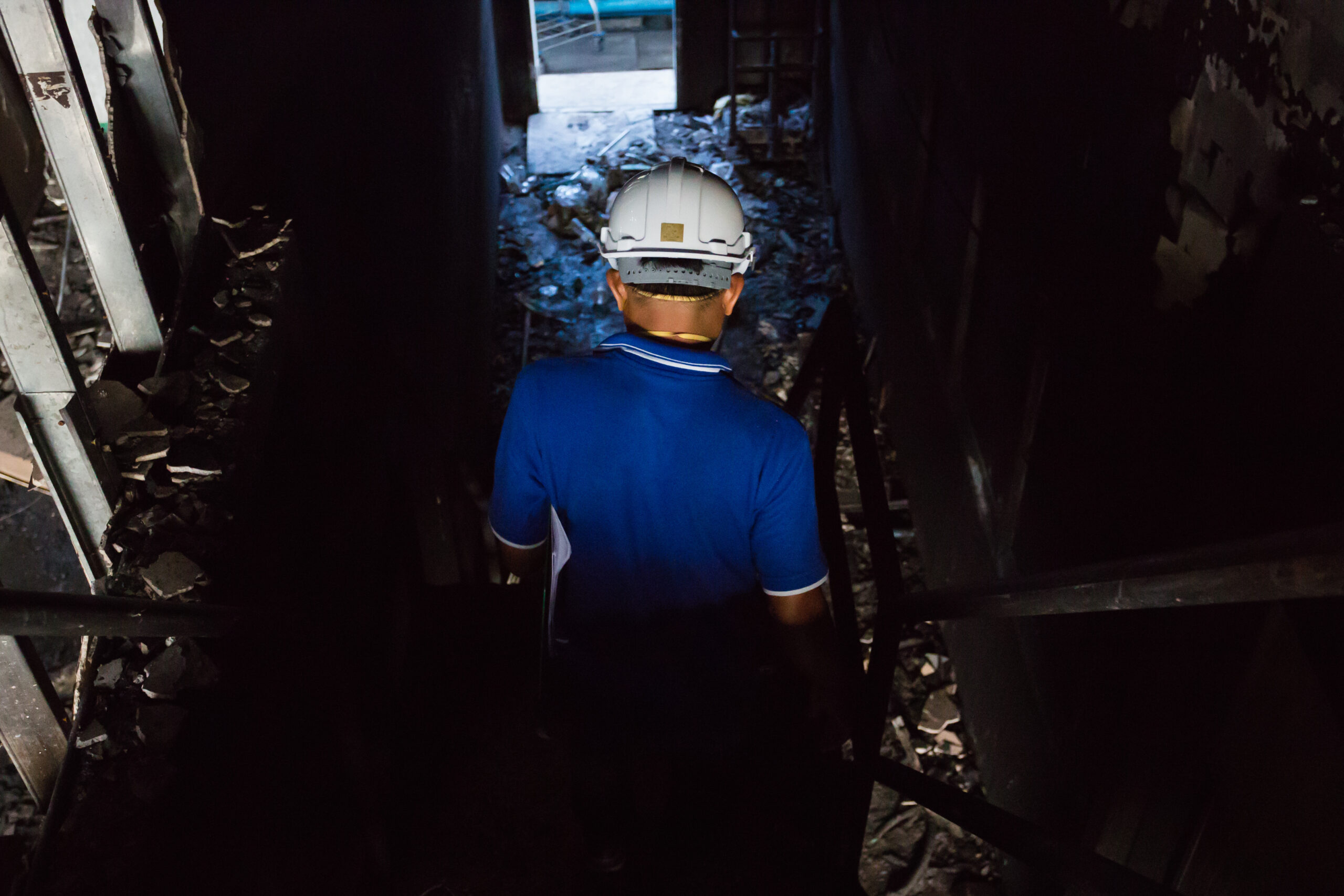 Rear view of safety officer entering charred hallway of fire-damaged site for post-incident inspection,Post-incident inspection, Workplace safety assessment.