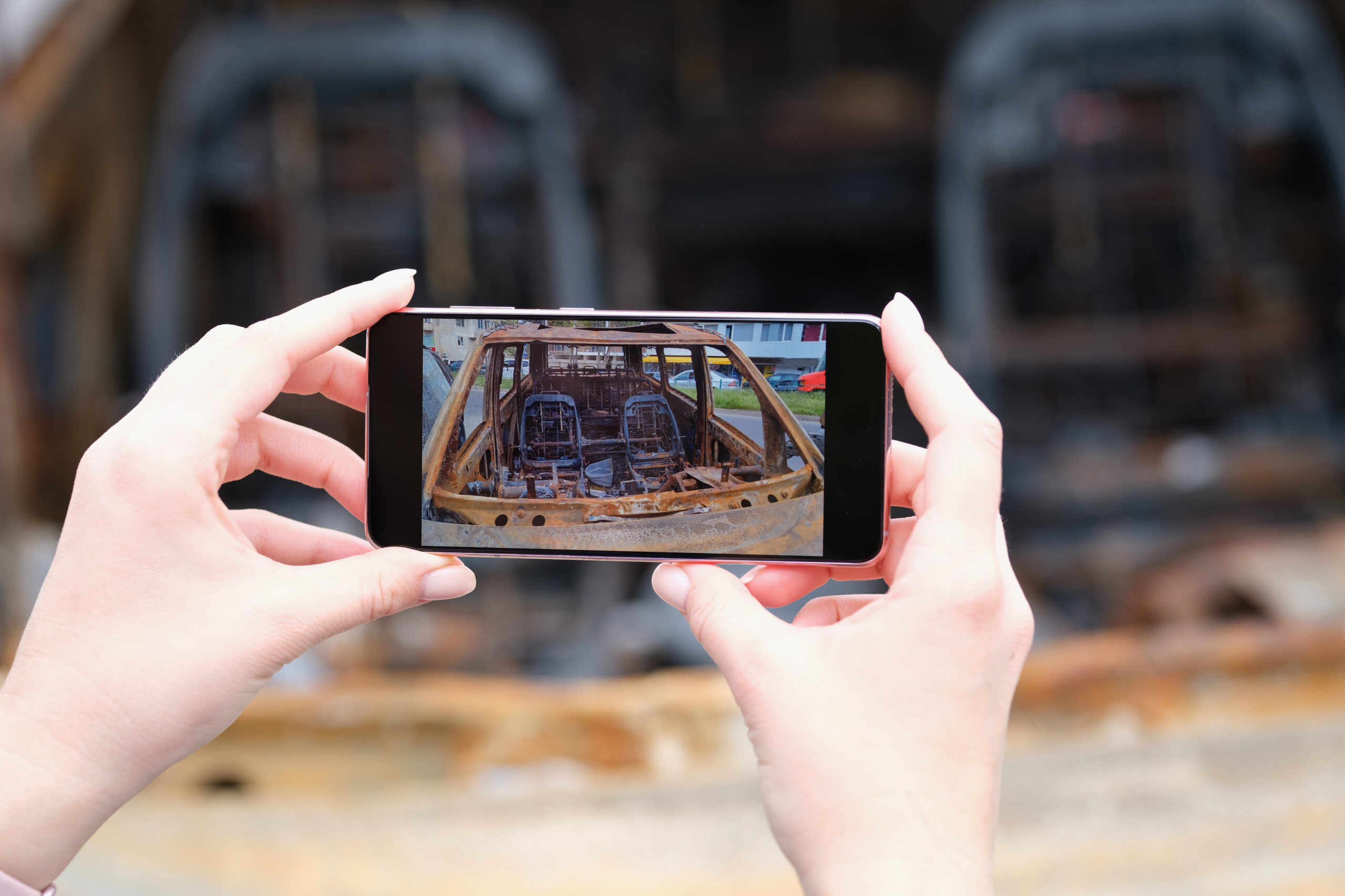 Insurance agent photographs burned-out car after it was set on fire. Owner or reporter examining burned out car after crime concept