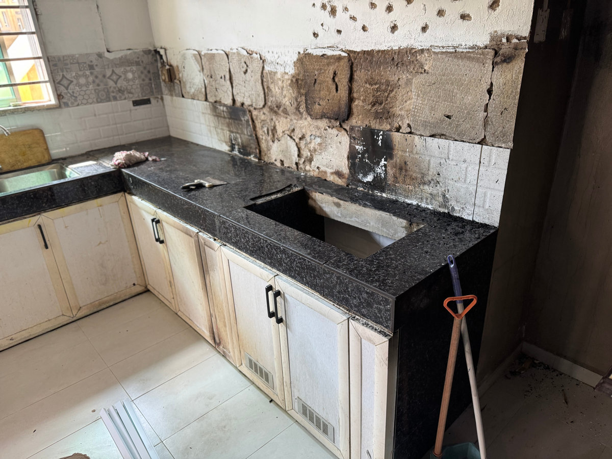 Burn marks from a fire scar the kitchen tabletop cabinet and the shelf area beneath it. The charred surfaces and blackened textures reveal the aftermath of intense heat and damage